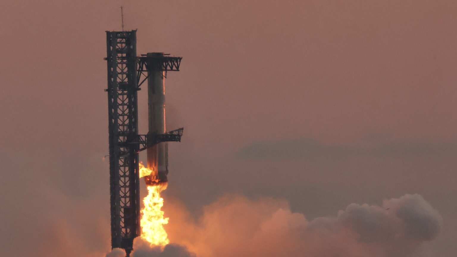 Super Heavy booster caught by the Starbase launch tower arms at dusk on Flight 5
